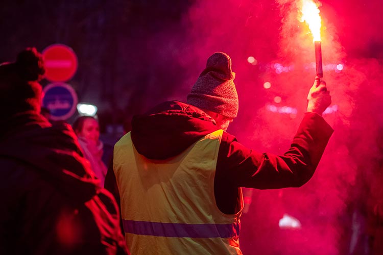 Gilet jaune levant une fusée éclairante rouge lors d'une manifestation nocturne — PUShAUNE