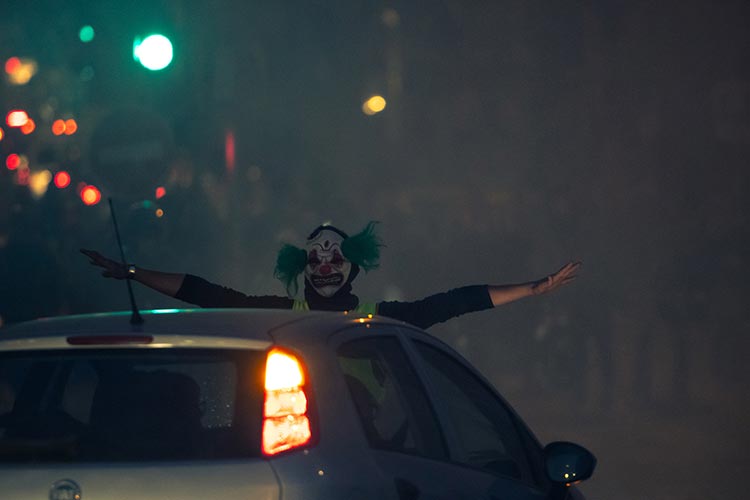 Manifestant masqué en clown sortant d'un toit ouvrant de voiture dans la nuit — PUShAUNE